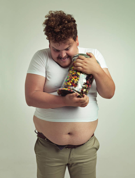 Candy, jar and crazy plus size man in studio for snacks, sweets and dessert in container. Comic, funny and isolated silly person with glass for unhealthy diet, sugar and treats on white background. - Photo, Image