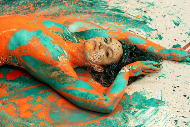 портрет и верхняя часть тела выразительной сексуальной женщины, лежащей обнаженной элегантно на полу в бирюзовом синем цвете абстрактно окрашенной женщины на брызгах земли - Фото, изображение