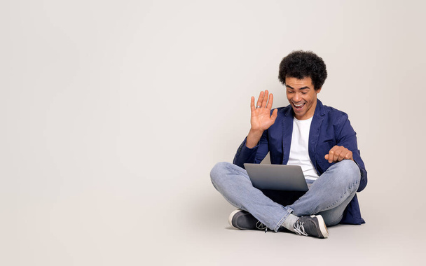 Homme d'affaires joyeux agitant la main lors d'une réunion en ligne sur un ordinateur portable tout en étant assis sur fond blanc - Photo, image