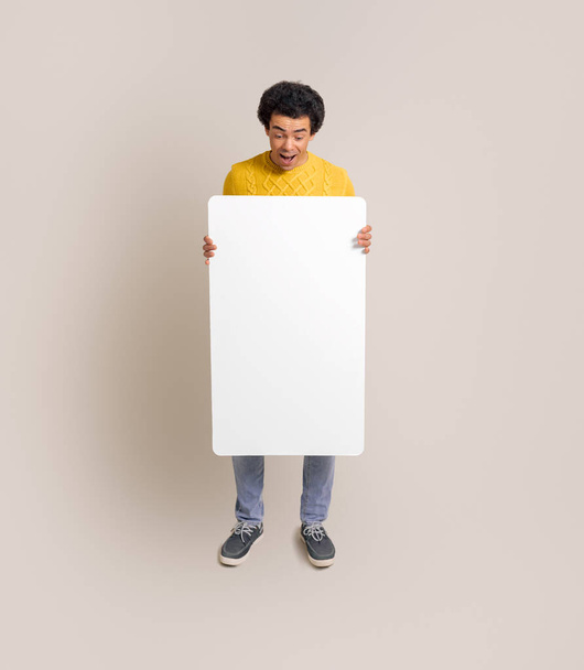 Täyspitkä innoissaan nuori myyntimies esittelee tyhjä juliste seisoessaan valkoinen tausta - Valokuva, kuva