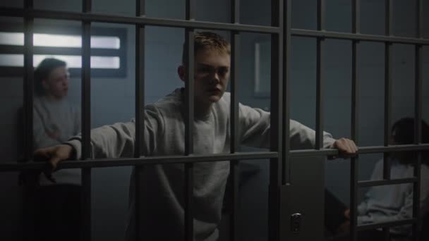 Portret różnych nastoletnich więźniów za metalowymi kratami w więziennej celi patrzących w kamerę. Wieloetniczni młodzi więźniowie siedzą w więzieniu. Ośrodek dla nieletnich lub zakład karny - Materiał filmowy, wideo