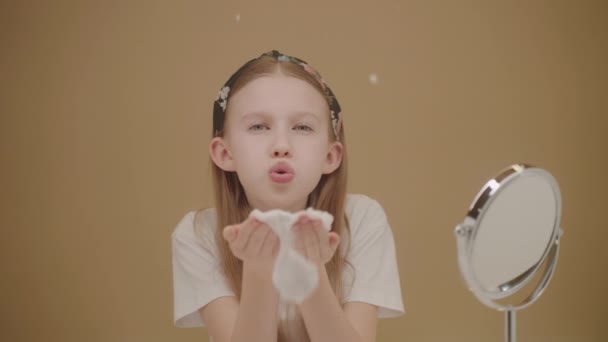 Happy Caucasian teen girl blows foamy soap bubbles towards camera while relaxing at her home. Playful young girl enjoying the little pleasures in life, smiling on Beige backdrop. Ad concept of beauty - Footage, Video