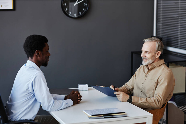 Side view portrait of smiling senior man talking to young candidate at job interview - Photo, Image