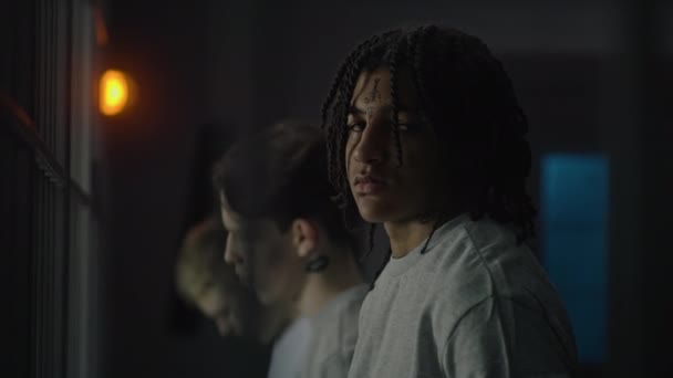 African American teenager stands near prison cell with Caucasian boys, looks at the camera. Young prisoner serves imprisonment term for crime in jail. Youth detention center or correctional facility. - Footage, Video