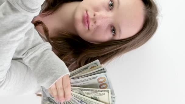 gazdag tinédzser lány integet egy rajongó 100 euró és 100 dolláros bankjegyek álló fehér háttér. mosolygós egy sport szürke pulóver laza barna haj meglepetés nyugodt gazdag gyermek - Felvétel, videó
