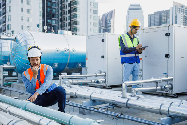 Asian man engineer using talkie walkie report working at rooftop building construction. Technician worker working checking hvac of office building. Engineering installing air conditioning system. - Foto, Bild