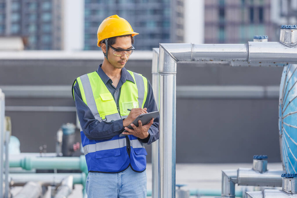Man engineer holding tablet working at rooftop building construction. Male technician worker working checking hvac of office building. Engineering installing large air conditioning system. - Zdjęcie, obraz