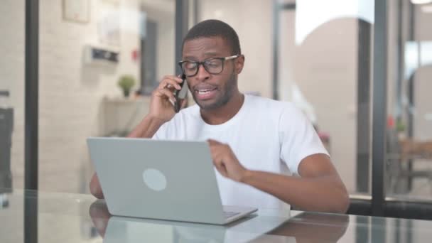 Afro-Américain Parler au téléphone tout en travaillant sur ordinateur portable - Séquence, vidéo