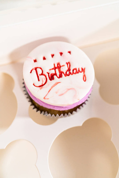 Los cupcakes de cumpleaños, bellamente adornados con decoraciones fondantes, se colocan cuidadosamente en cajas de papel blanco, listas para su gran presentación. - Foto, imagen