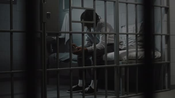 African American young prisoner eats disgusting prison food from iron bowl sitting on bed in prison cell. Teenage criminal, inmate serves imprisonment term for crime in jail. Youth detention center. - Footage, Video