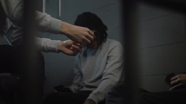 Drie multi-etnische tieners spelen kaarten in de cel. Jonge gevangenen zitten gevangenisstraf uit voor misdaden in de gevangenis. Jeugddetentiecentrum of gevangenis. Zicht door metalen staven. - Video
