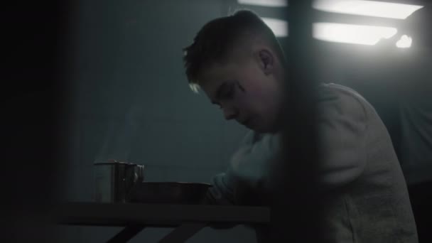 Kaukasischer jugendlicher Verbrecher isst Gefängnisessen am Tisch in der Gefängniszelle. Junger Häftling verbüßt Haftstrafe im Jugendgefängnis Ein weiterer Häftling blickt auf Fenster im Hintergrund. - Filmmaterial, Video
