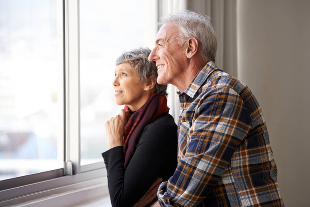 Mature couple, man and woman in window of house, home and retirement holiday with happiness. Smile, elderly people and marriage for bonding, commitment and love in vacation for female and male person. - Photo, Image