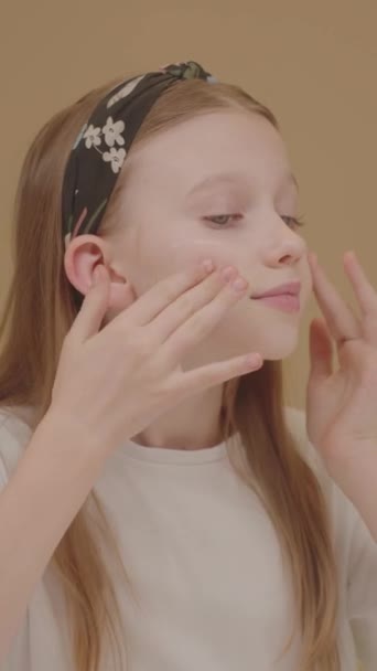 素敵な若い女の子はフェイスクリームを着ています. かわいいブロンドの女の子は鏡を見て,頬に保湿剤を加えます. 輝く肌で純粋に。 十代の若者とインフルエンサーのための美しさとスキンケアの概念. 化粧品 広告. - 映像、動画