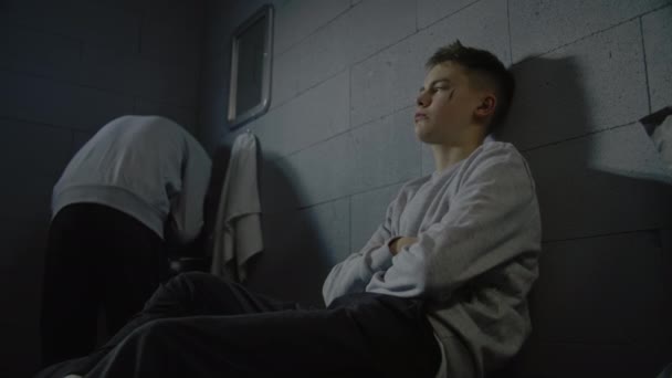 Aufgebrachte kaukasische Teenager sitzen auf dem Bett in der Gefängniszelle. Ein afroamerikanischer Häftling wäscht sein Gesicht im Waschbecken. Junge Kriminelle verbüßen eine Gefängnisstrafe. Jugendstrafanstalt. - Filmmaterial, Video