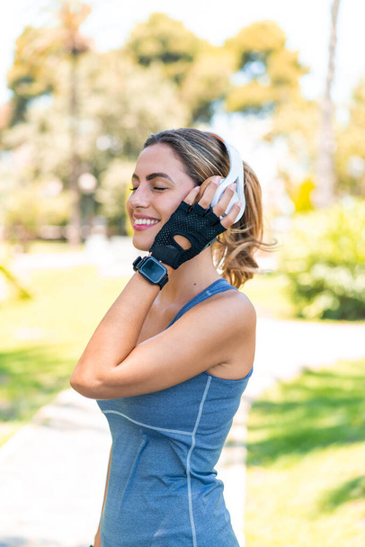 Νεαρή ξανθιά γυναίκα σε εξωτερικούς χώρους φορώντας αθλητικά ρούχα και ακούγοντας μουσική με ακουστικά - Φωτογραφία, εικόνα