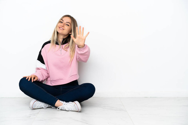 Молодая женщина сидит на полу в помещении и считает пятерых с пальцами - Фото, изображение