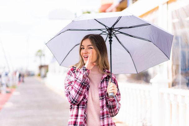 Joven mujer rumana bonita sosteniendo un paraguas al aire libre susurrando algo - Foto, Imagen