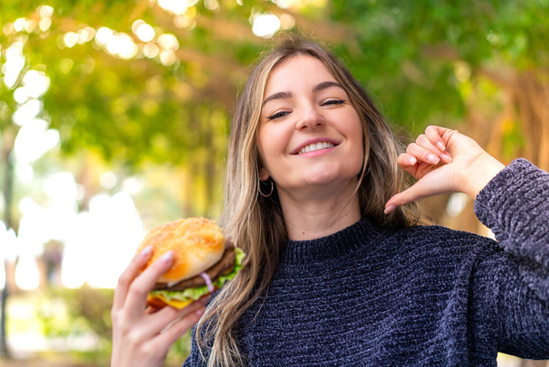 Fiatal csinos román nő kezében egy hamburger a szabadban büszke és önelégült - Fotó, kép