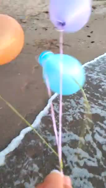 Tre palline gonfiabili colorate sullo sfondo del mare su forti venti. Persona che gioca con palloni aerostatici multicolori in mano sulle onde del mare sullo sfondo sulla spiaggia sabbiosa. Divertimento intrattenimento Verticale - Filmati, video