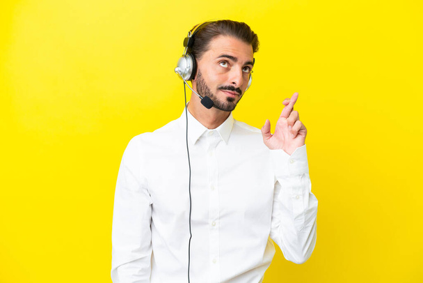 Telemarketer kaukasischen Mann arbeitet mit einem Headset isoliert auf gelbem Hintergrund mit Daumen drücken und wünschen das Beste - Foto, Bild