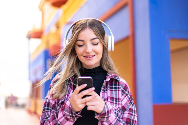 Junge hübsche Rumänin im Freien hört Musik und schaut auf ihr Handy - Foto, Bild