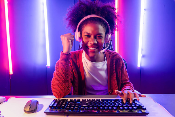 Streamer gier, afrykańska dziewczyna gra online walki z Esport wykwalifikowany zespół noszenia słuchawek w neonowym kolorze oświetlenie pokoju. Rozmawianie z innymi graczami struganie strategii, aby wygrać konkurentów. Tastemaker. - Zdjęcie, obraz