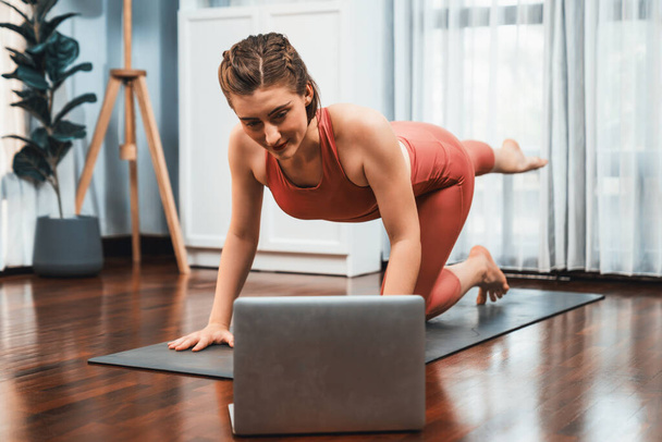 Rugalmas és ügyes nő sportruházatban jóga pozícióban meditációs testtartásban gyakorló szőnyegen otthon. Egészséges jókedv otthon jóga online tréning békés elmével és nyugalommal. - Fotó, kép