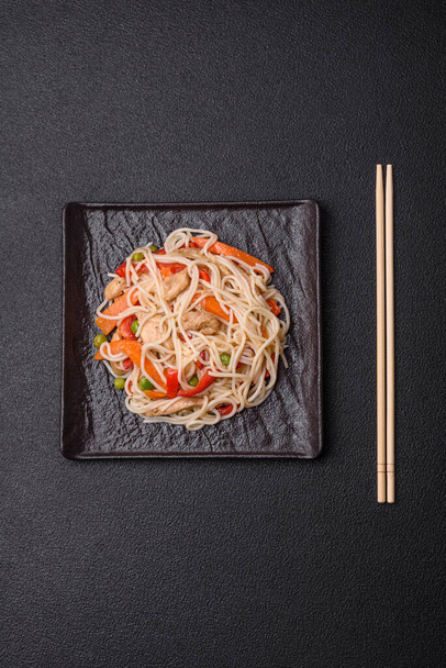 Νόστιμα νούντλς ρυζιού ή udon με κοτόπουλο, καρότα, πιπέρι, αλάτι, μπαχαρικά και βότανα σε σκούρο μπετόν φόντο - Φωτογραφία, εικόνα