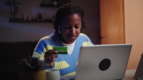 Молодая черная американка с помощью кредитной карты на ноутбуке сидит на столе ночью в номере. Счастливый, жизнерадостный клиент совершает покупки онлайн в интернет-магазине.. - Кадры, видео