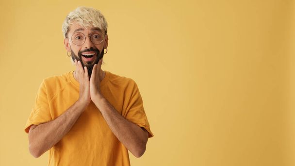 Guy with glasses, dressed in yellow T-shirt, looks away at advertising space, surprised, wow, isolated on yellow background in studio - Foto, immagini