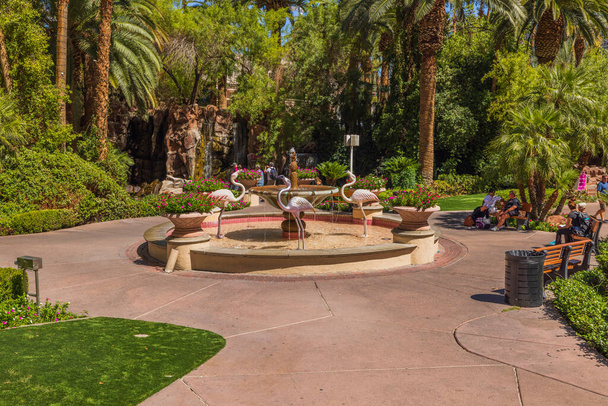 Veduta di persone che passeggiano attraverso il giardino tropicale del casinò Flamingo Hotel, con vista su una fontana e sculture di fenicotteri rosa. Las Vegas. Stati Uniti.  - Foto, immagini