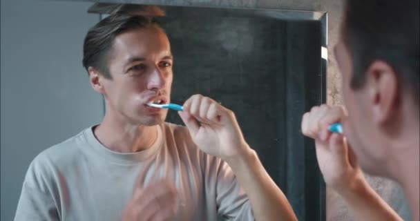 Guy putzt sorgfältig seine Zähne im Badezimmer, hat aber Probleme. Der Mensch hat ein Problem mit Schmerzen aufgrund überempfindlichen Zahnfleisches. Dieses häufige Problem macht Jungs während ihrer täglichen Mundhygiene-Routine unangenehm - Filmmaterial, Video
