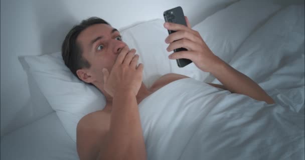 Facet leży w łóżku od rana i otwiera telefon komórkowy, czyta szokujące wiadomości. Szokujące nagłówki skłaniają nas do myślenia o przyszłości. Szokujące fakty na ekranie sprawiają, że ponownie rozważyć swoje plany na dzień - Materiał filmowy, wideo