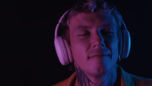 Gros plan de beau mec avec tatouage sur le cou dansant à la musique dans les écouteurs dans la chambre avec lumière au néon - Séquence, vidéo