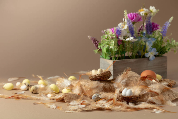 Paascompositie met eieren, veren en lentebloemen op een beige achtergrond. Kopieerruimte. - Foto, afbeelding