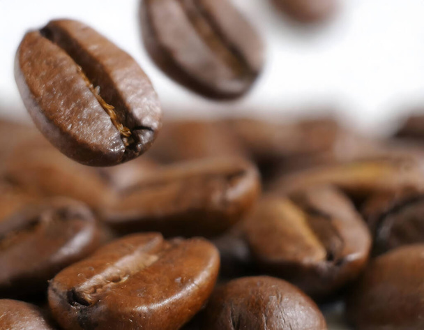 さまざまな形やサイズの白い背景にコーヒー豆の山に落ちるコーヒー豆のクローズアップ,激しい茶色の色,ゆっくりとした動きで落ちて小さなヒープを形成する - 写真・画像