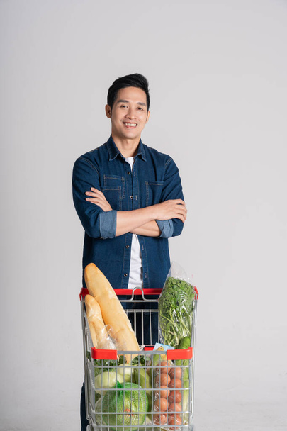 Feliz sorridente homem empurrando carrinho de supermercado isolado no fundo branco - Foto, Imagem