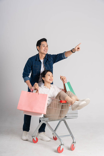 Щаслива усміхнена пара штовхає візок супермаркету ізольовано на білому тлі - Фото, зображення