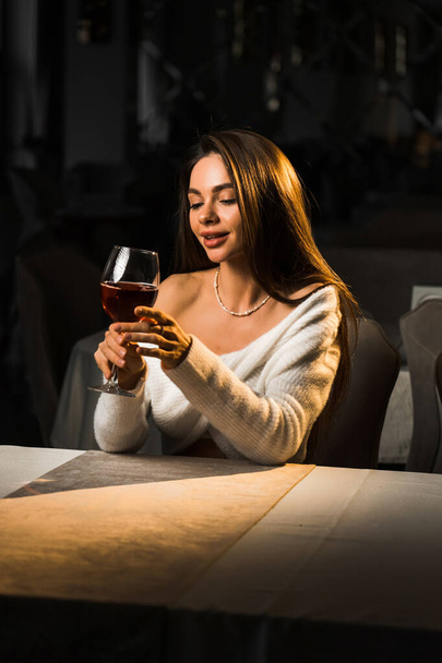 Молодая женщина держит бокал вина. Женщина пьет вино в ресторане. - Фото, изображение