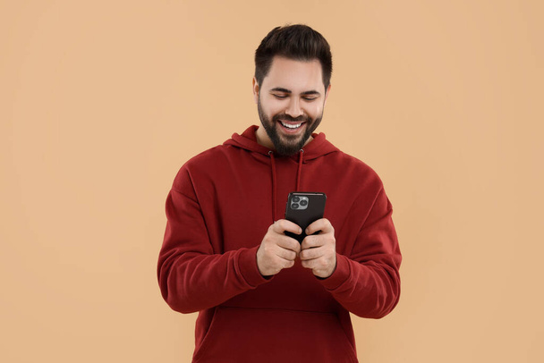 Happy young man using smartphone on beige background - 写真・画像