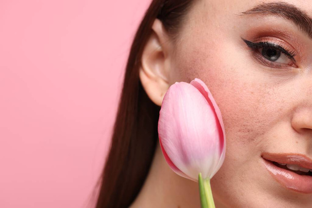 Beautiful woman with fake freckles and tulip on pink background, closeup. Space for text - Foto, imagen