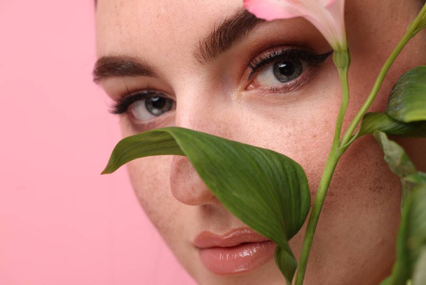 Beautiful woman with fake freckles and flower on pink background, closeup - Foto, imagen