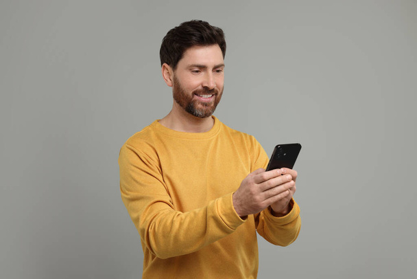Smiling man with smartphone on grey background - Foto, afbeelding