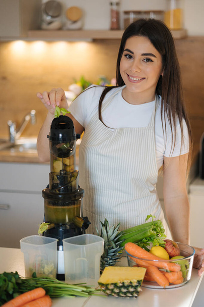 Proces atrakcyjnej kobiety zrobić świeży sok w sokowirówce. Kobieta w fartuchu w kuchni. Wysokiej jakości zdjęcie - Zdjęcie, obraz