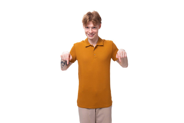 Ένας νεαρός όμορφος κοκκινομάλλης με ένα κούρεμα και ένα τατουάζ στο μπράτσο του λέει τα νέα. έννοια της διαφήμισης. - Φωτογραφία, εικόνα
