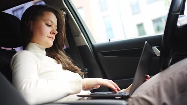 Joven mujer de negocios que trabaja en el ordenador portátil sentado en un coche detrás del volante, lugar de trabajo del coche. Imágenes de alta calidad 4k - Metraje, vídeo