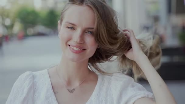Ein Video, in dem eine schöne junge Frau in einem weißen Kleid lächelt, ihre Haare berührt und in die Kamera blickt - Filmmaterial, Video