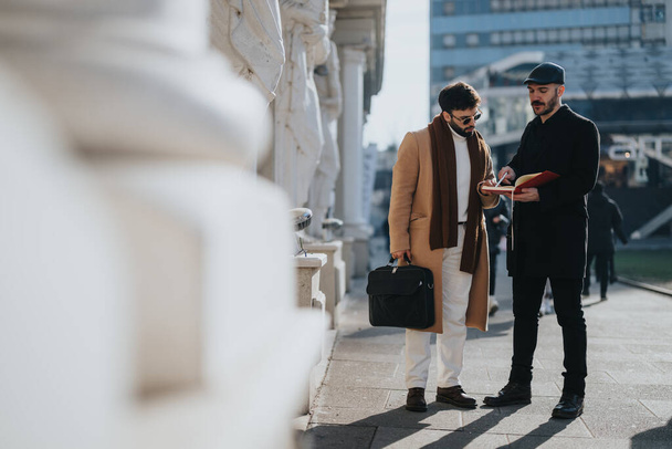 Two stylish businessmen in winter coats engaging in a discussion with a notebook outdoors, embodying teamwork and professionalism. - Photo, Image