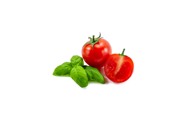 Rijp rode tomaat in tweeën gesneden naast basilicum op een witte achtergrond - Foto, afbeelding